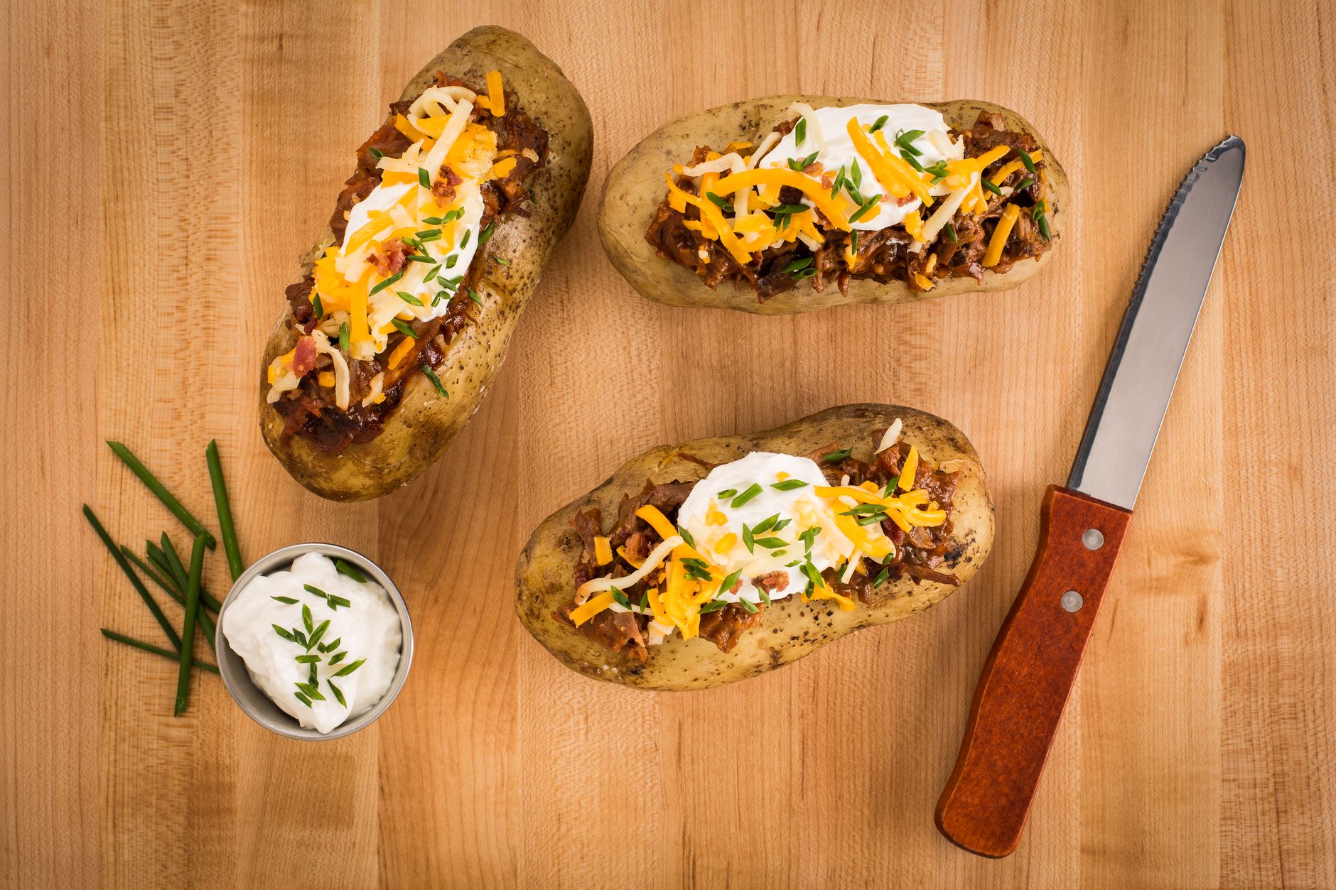 Mouth watering loaded baked potatoes with cheese, sour cream, and chives on a wooden surface, illustrating What Is an Ice Cream Potato, and Is It a Real Thing