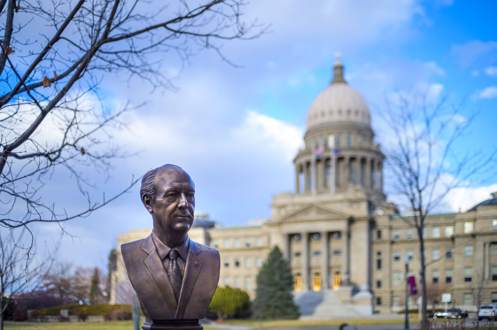 Bronze bust located in park near historic Idaho State Capitol with columns and dome against cloudy blue sky in Boise, illustrating Where Do Boise's Food Trucks Gather? A Straight A